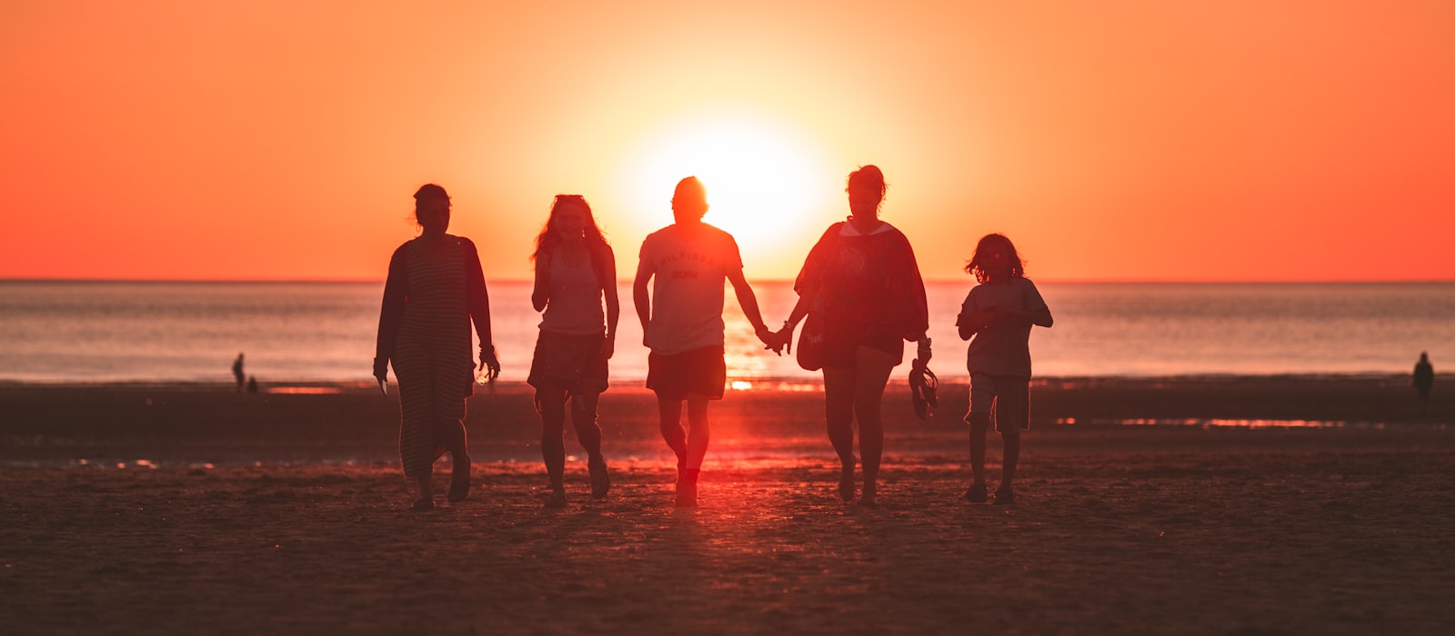 Silhouettes d'une famille marchant sur une plage au coucher du soleil