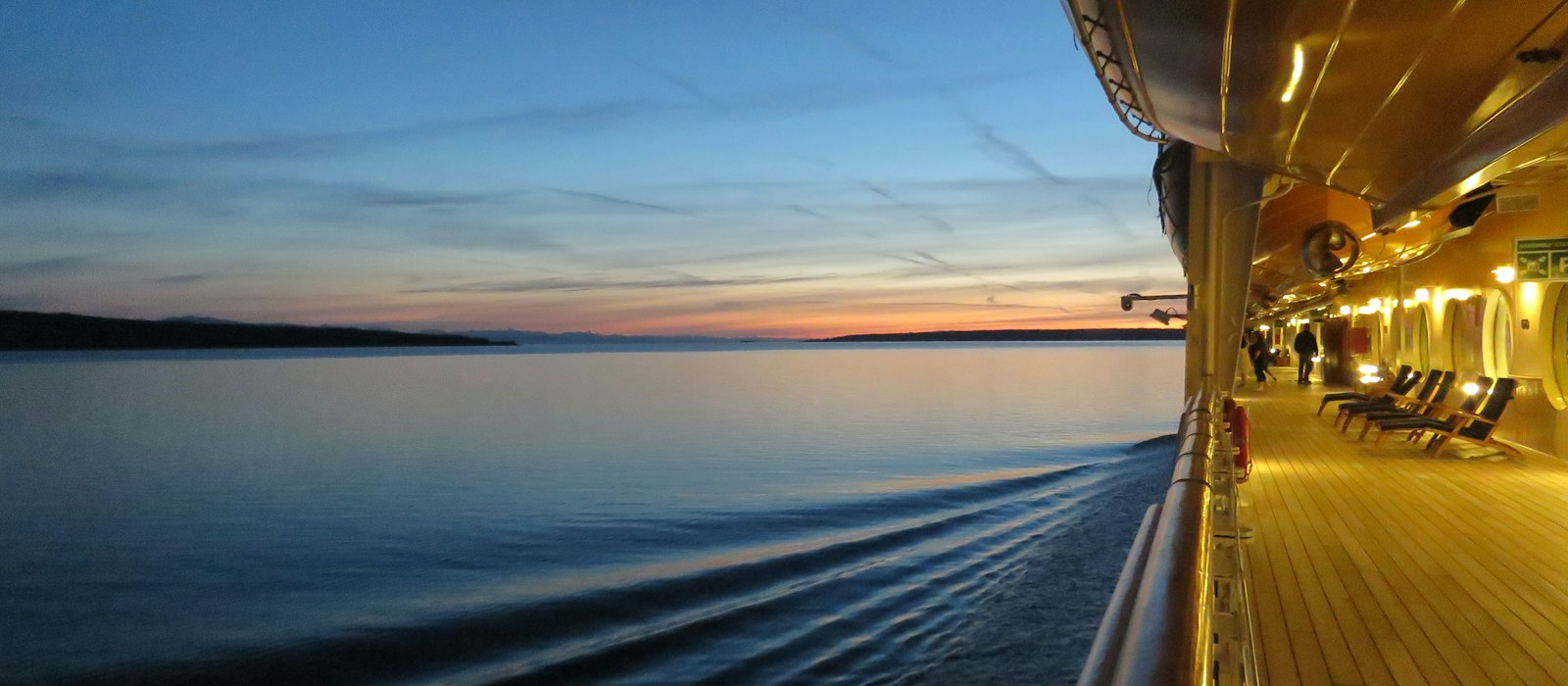 Le pont promenade d'un navire de croisière au crépuscule, face à une mer calme et à l'horizon