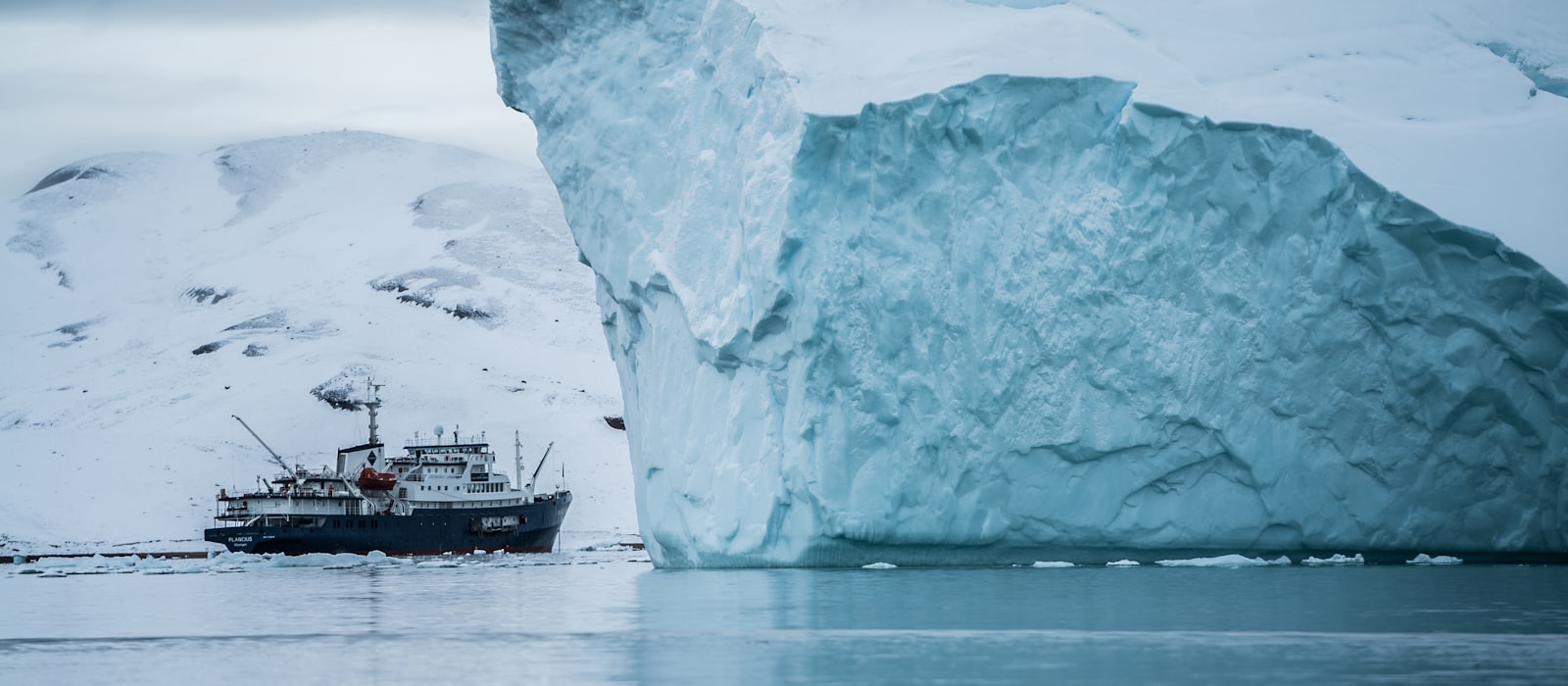 Petit navire d'expédition mouillant au pied d'un iceberg en zone polaire
