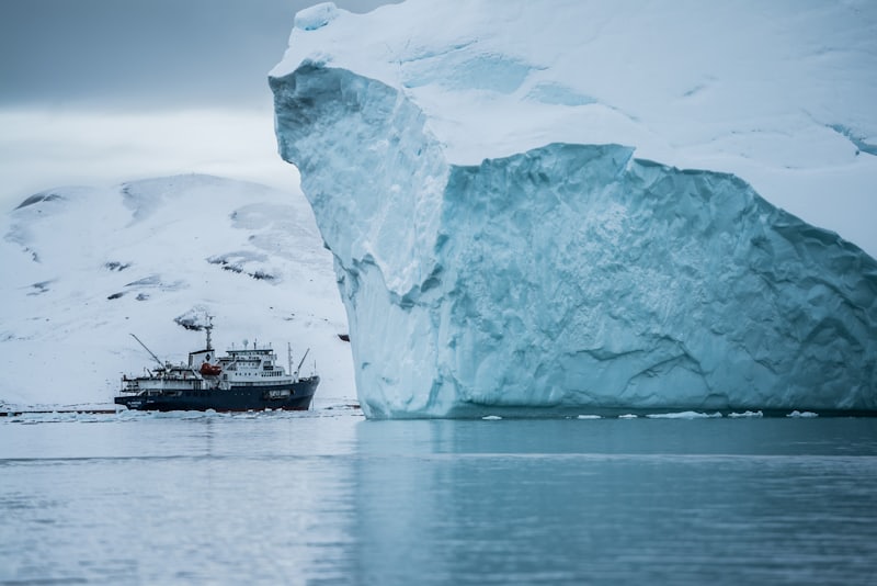 Petit navire d'expédition mouillant au pied d'un iceberg en zone polaire