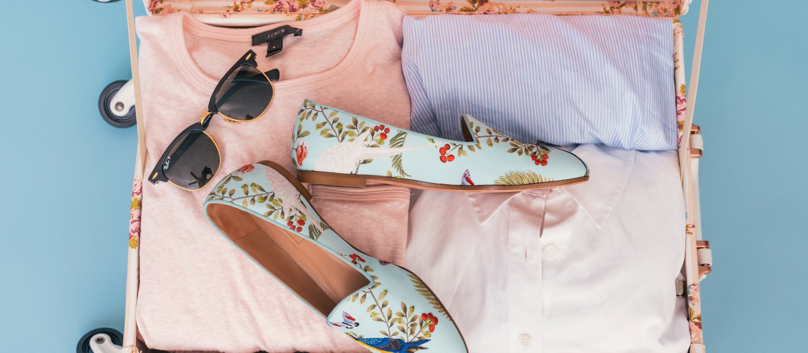 Une valise ouverte avec des vêtements pliés, des lunettes de soleil et une paire de mocassins