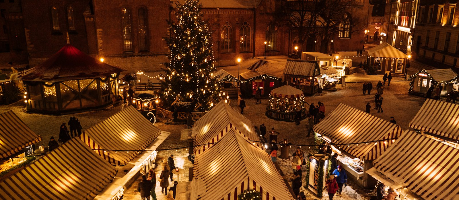 Un marché de Noël illuminé la nuit, ses chalets et son grand sapin décoré