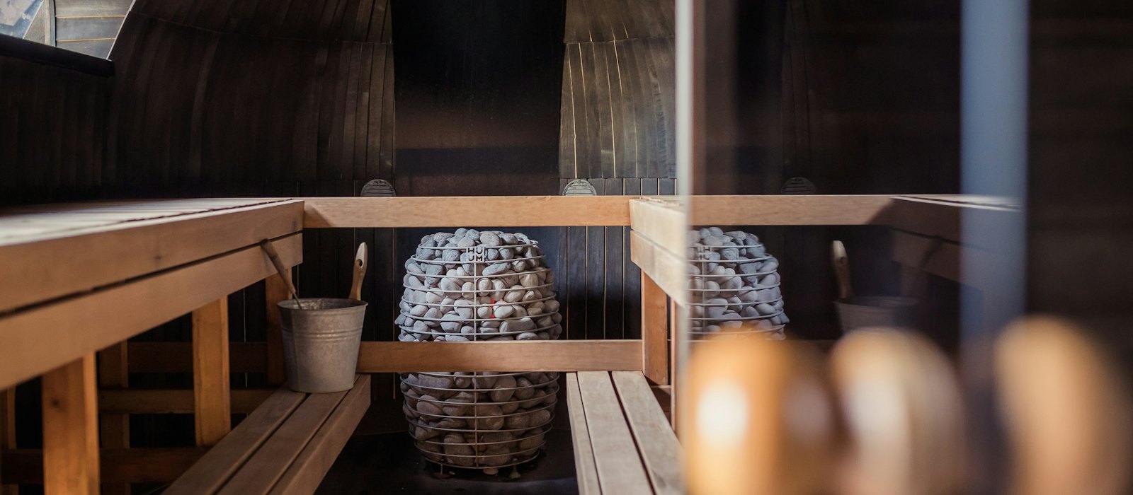 L'intérieur d'un sauna en bois, avec ses banquettes et son poêle à pierres