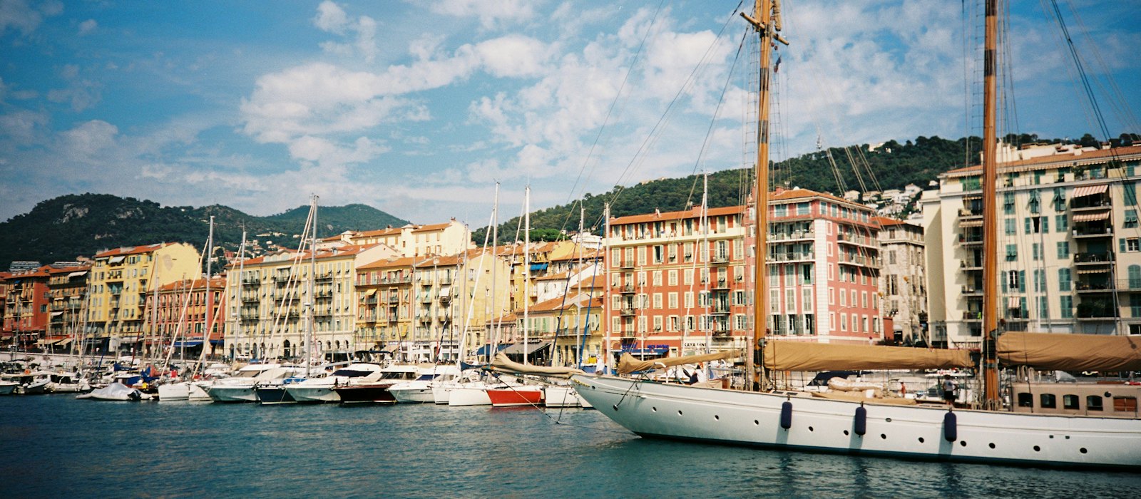 Un voilier à deux mâts amarré dans le port Lympia de Nice, devant les façades colorées du quai