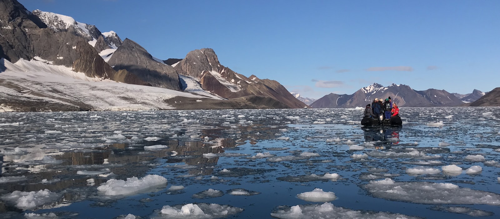 Zodiac d'expédition progressant dans la banquise devant des montagnes arctiques