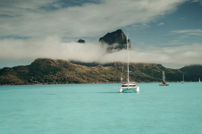 Des catamarans au mouillage dans le lagon turquoise de Bora Bora, au pied du mont Otemanu pris dans les nuages