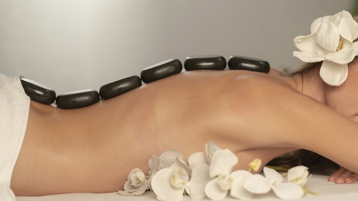 Un massage aux pierres chaudes posées le long du dos, avec des orchidées blanches sur la table de soin