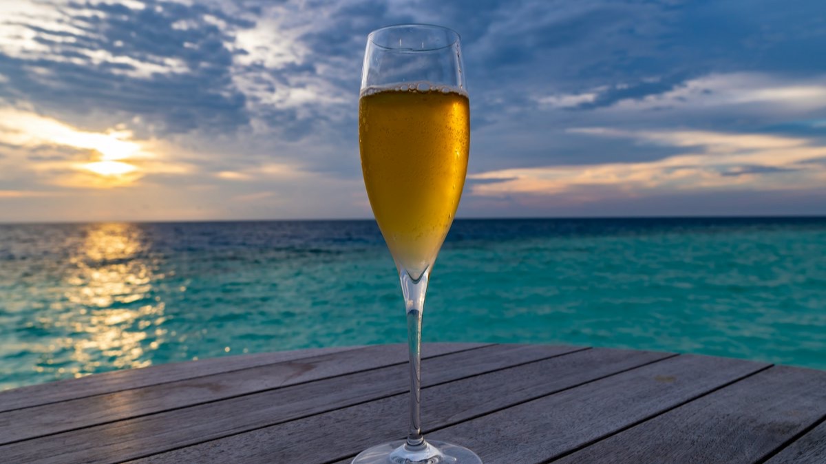 Une flûte de champagne posée sur une table en bois, face à la mer au coucher du soleil