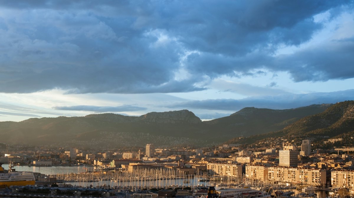 La ville et le port de Toulon au pied des collines, sous un ciel nuageux