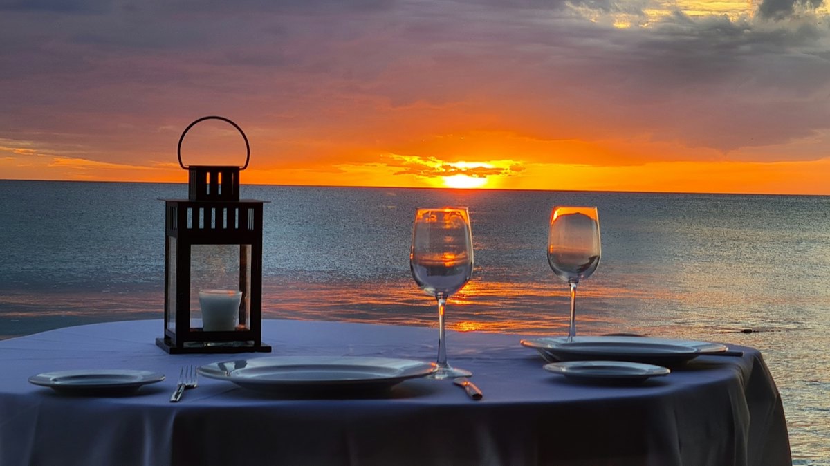 Une table dressée pour deux, avec une lanterne et deux verres de vin, face à la mer au coucher du soleil