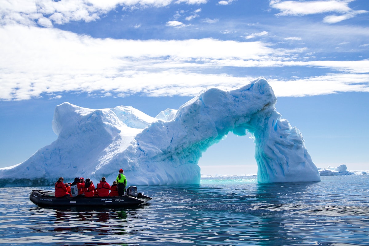 Zodiac d'expédition et passagers en parkas face à une arche de glace en Antarctique