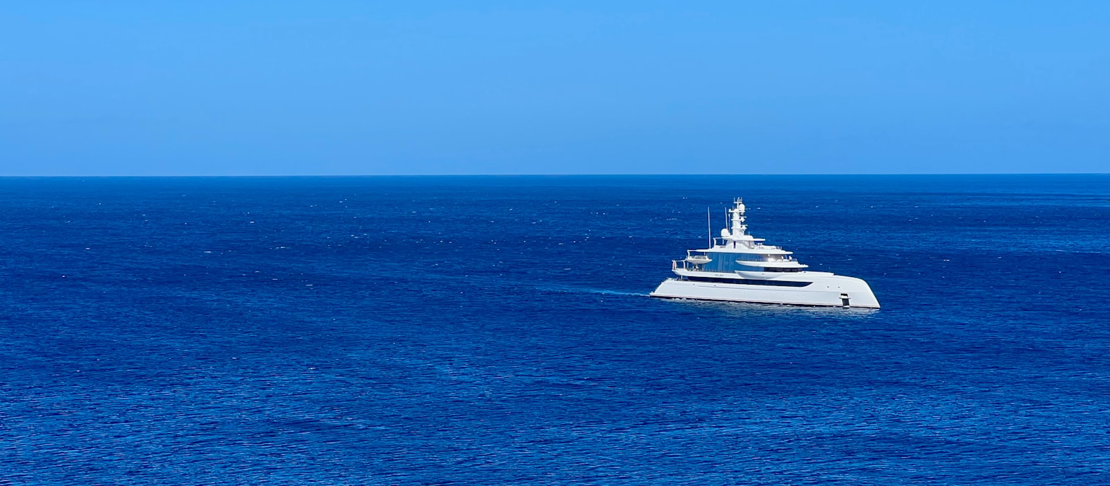 Yacht blanc naviguant seul sur une mer bleue profonde, horizon dégagé
