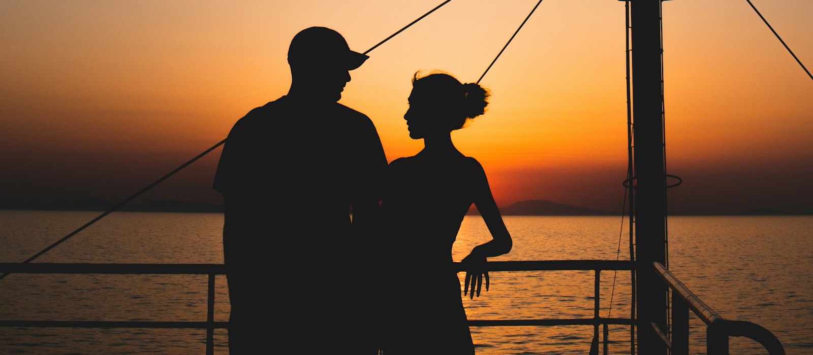 Un couple en silhouette sur le pont d'un navire, face à la mer au coucher du soleil