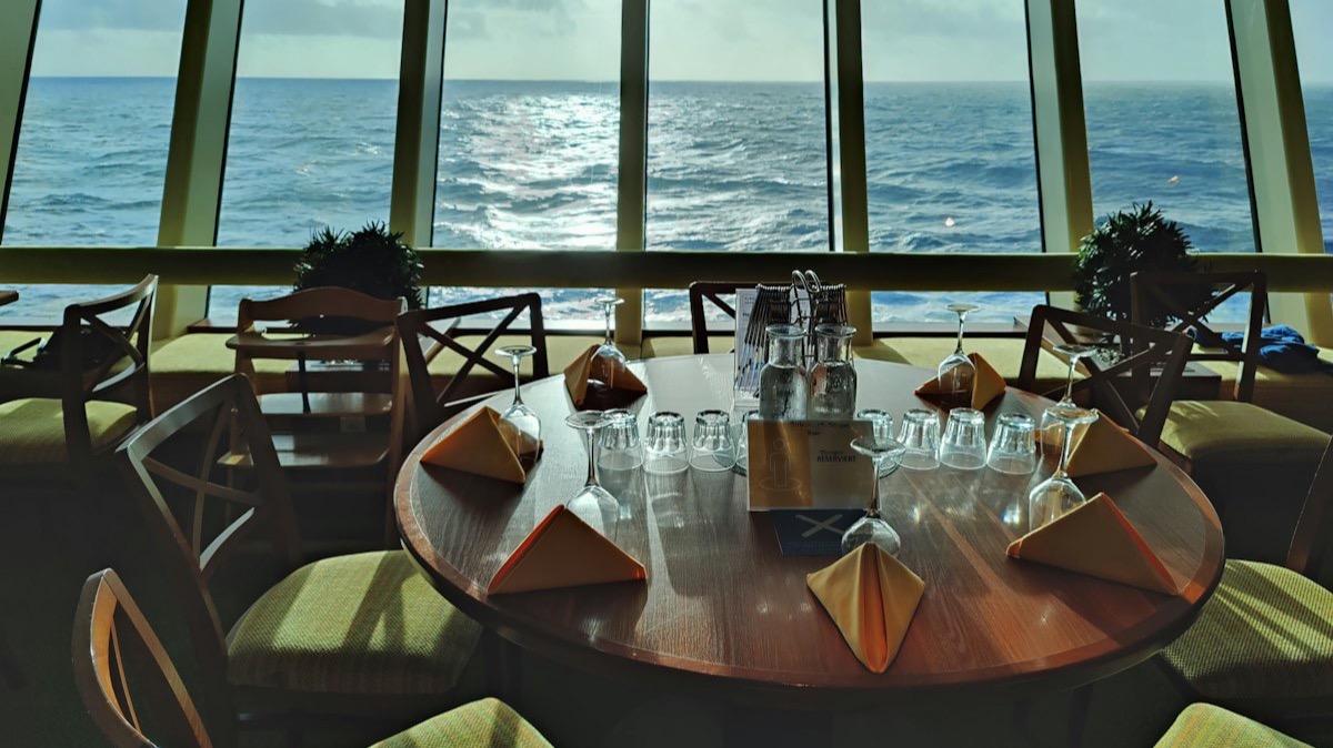 La salle d'un restaurant panoramique à bord d'un navire, ses tables dressées face aux baies vitrées