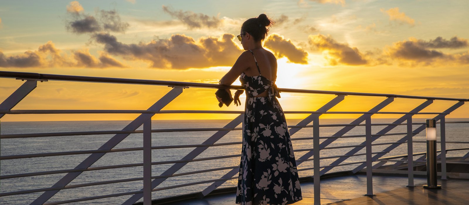 Une voyageuse seule accoudée au bastingage d'un navire, face à la mer au coucher du soleil