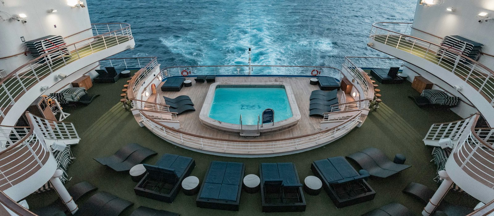 La piscine du pont arrière d'un navire de croisière, entourée de transats, face au sillage en pleine mer