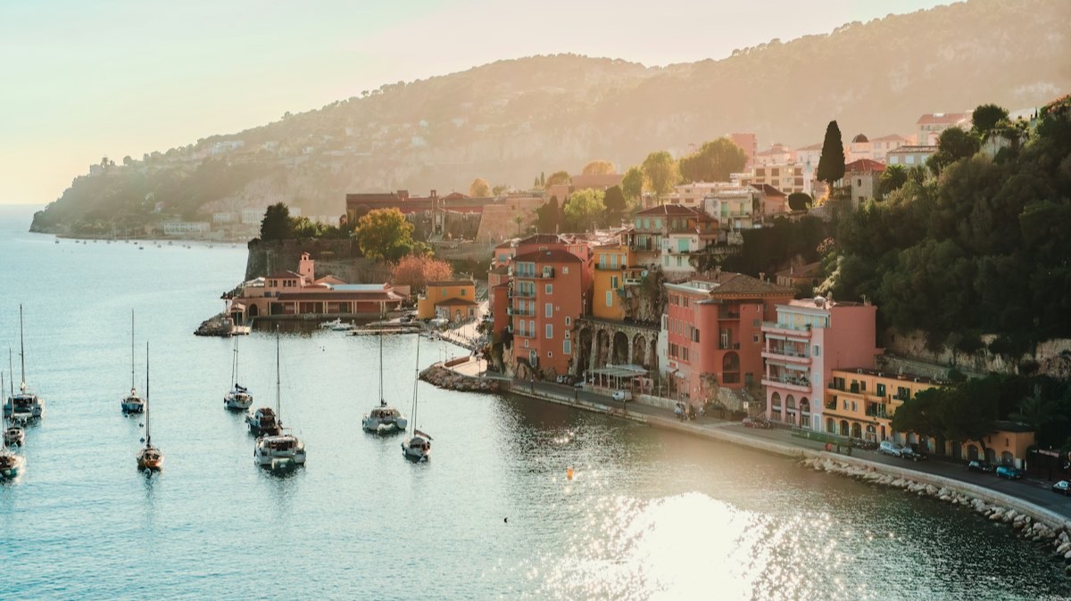 Des voiliers au mouillage dans la rade de Villefranche-sur-Mer, devant les maisons colorées du village