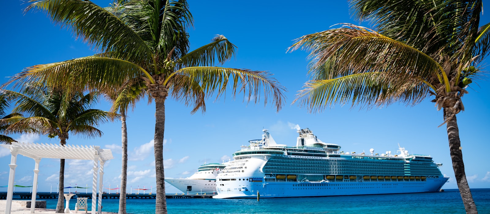 Grand navire de croisière à quai devant une plage des Caraïbes bordée de cocotiers