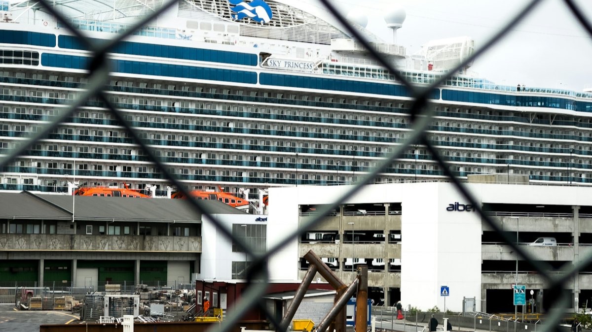 Un paquebot de croisière à quai, vu à travers le grillage d'une zone de travaux