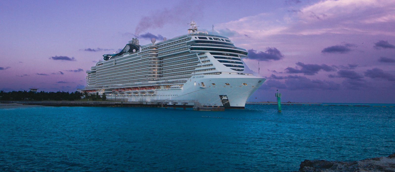 Un grand paquebot de croisière blanc au mouillage près d'une côte, sous un ciel de crépuscule