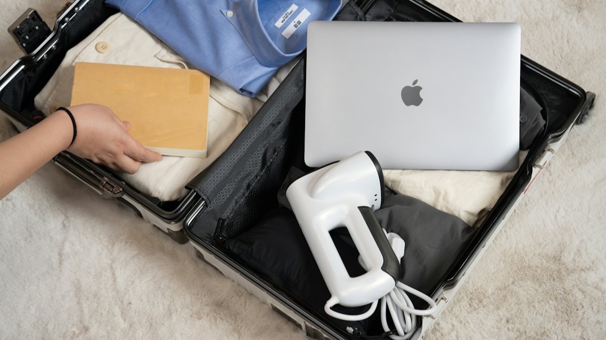 Une valise ouverte avec des chemises, un ordinateur portable et un défroisseur à vapeur