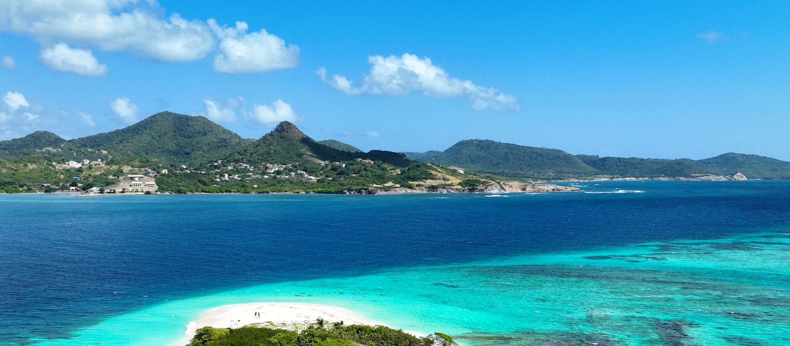 Îlot bordé de récifs turquoise devant une île montagneuse des Petites Antilles