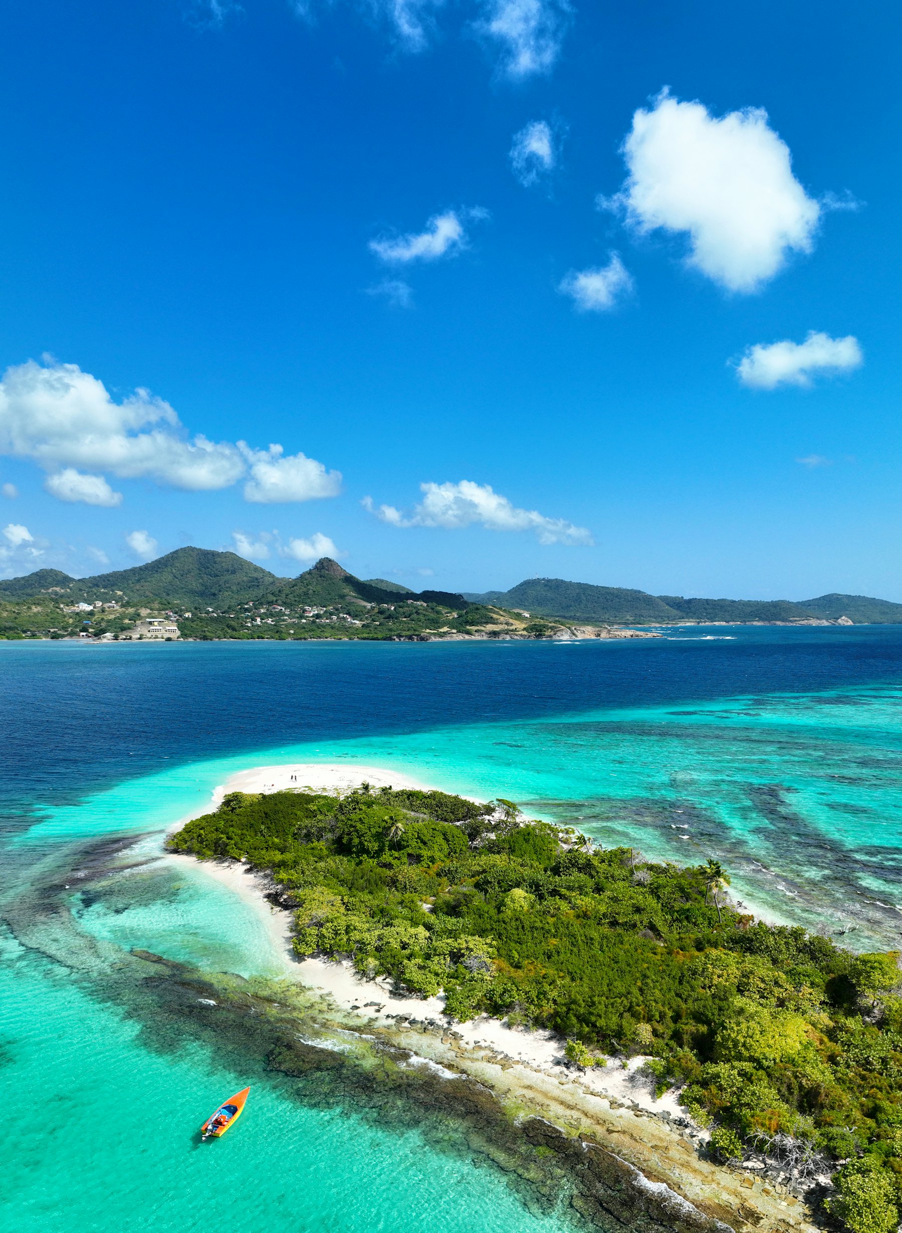 Îlot bordé de récifs turquoise devant une île montagneuse des Petites Antilles