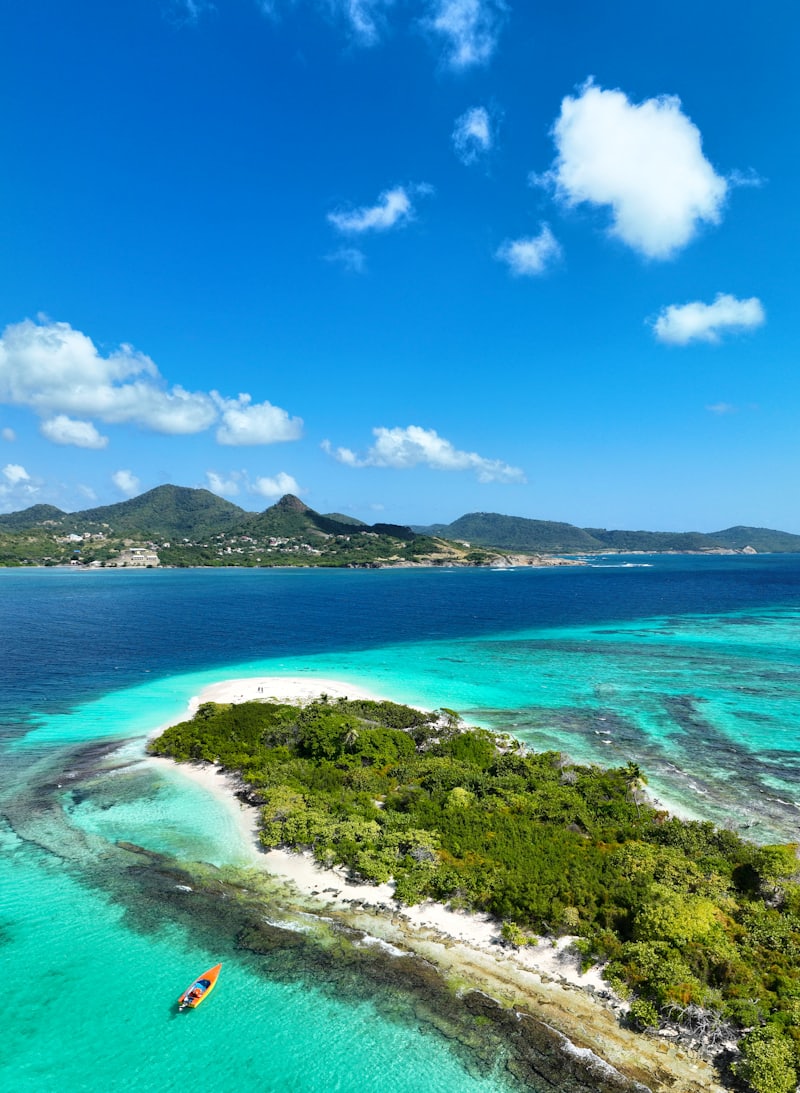 Îlot bordé de récifs turquoise devant une île montagneuse des Petites Antilles