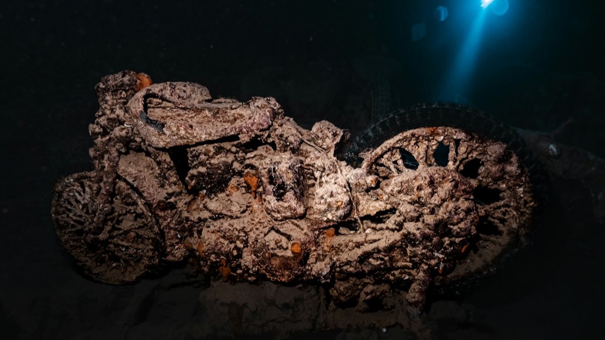 Une moto couverte de concrétions dans la cale sombre d'une épave, éclairée par un rayon de lumière