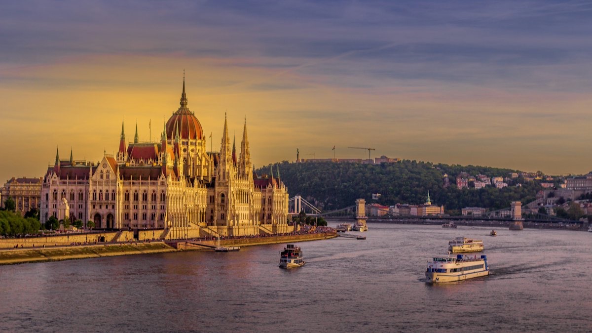 Le Parlement de Budapest au bord du Danube, au coucher du soleil, avec des bateaux sur le fleuve