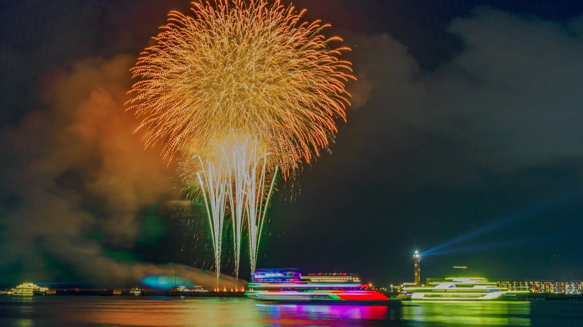 Un feu d'artifice doré au-dessus d'un port où sont amarrés des bateaux illuminés