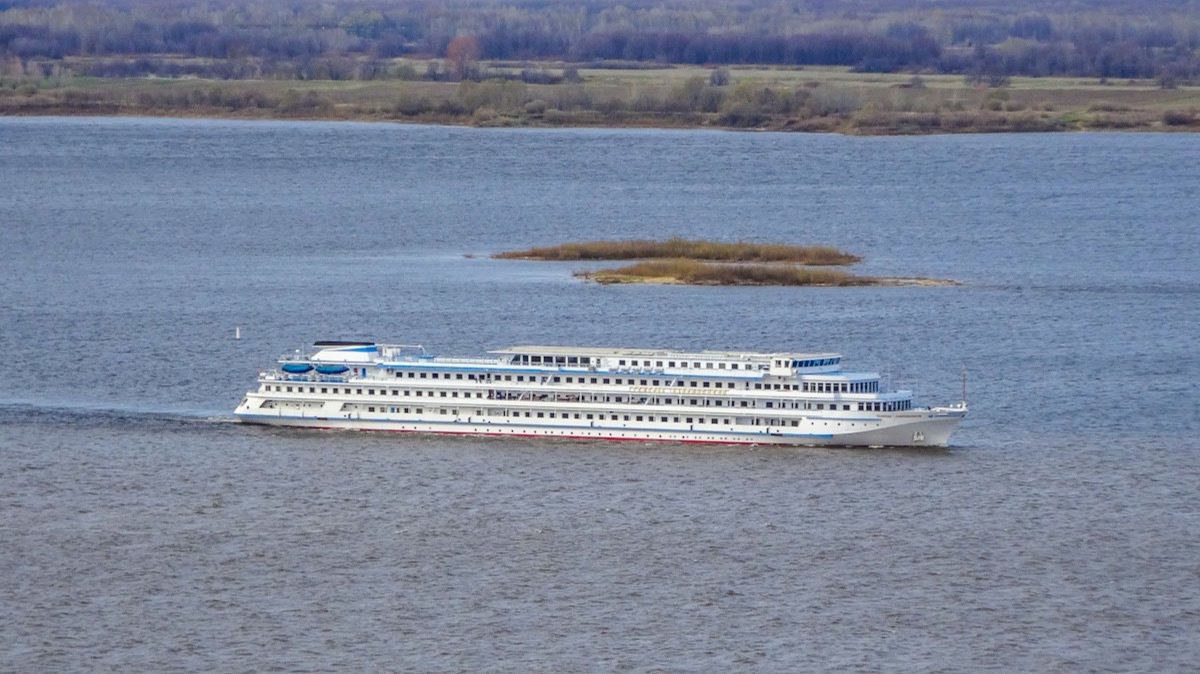 Un bateau de croisière fluviale blanc sur un large fleuve bordé de collines