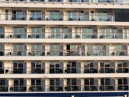 Façade d'un navire de croisière : rangées de cabines à balcon privé, un passager accoudé