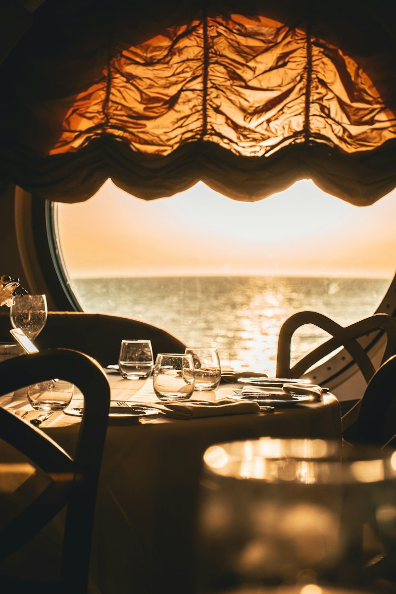 Table dressée devant un grand hublot rond ouvert sur la mer au coucher du soleil