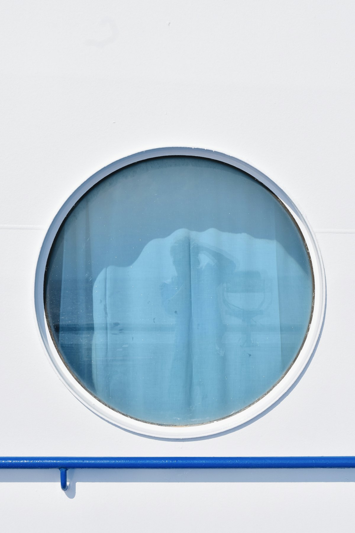 Hublot rond sur une cloison blanche donnant sur la mer