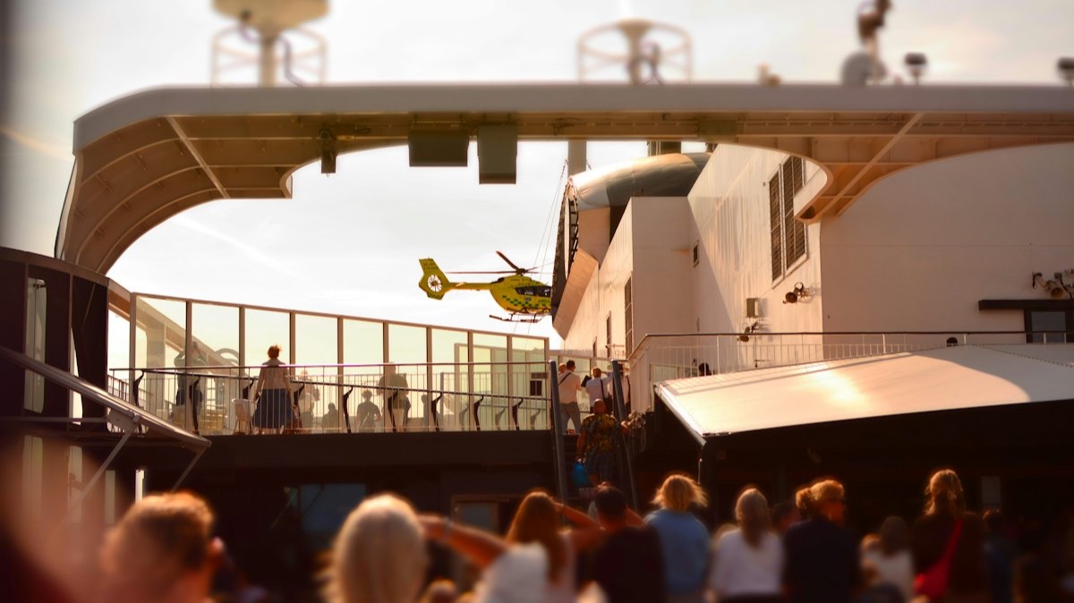 Un hélicoptère jaune près du pont d'un navire de croisière, observé par des passagers